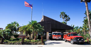 Fire station 6 has palm trees planted in the front of the American flag. Both engine 66 and ocean rescue 66 are parked in the driveway.