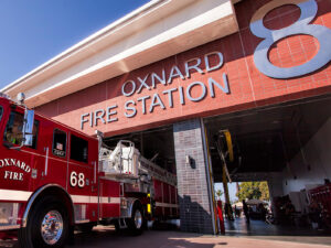A pristine fire engine 68 is parked halfway in one of the large garage doors of fire station 8 on a beautiful sunny day.