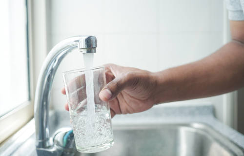 A hand filling a glass cup with clean water from the tap.